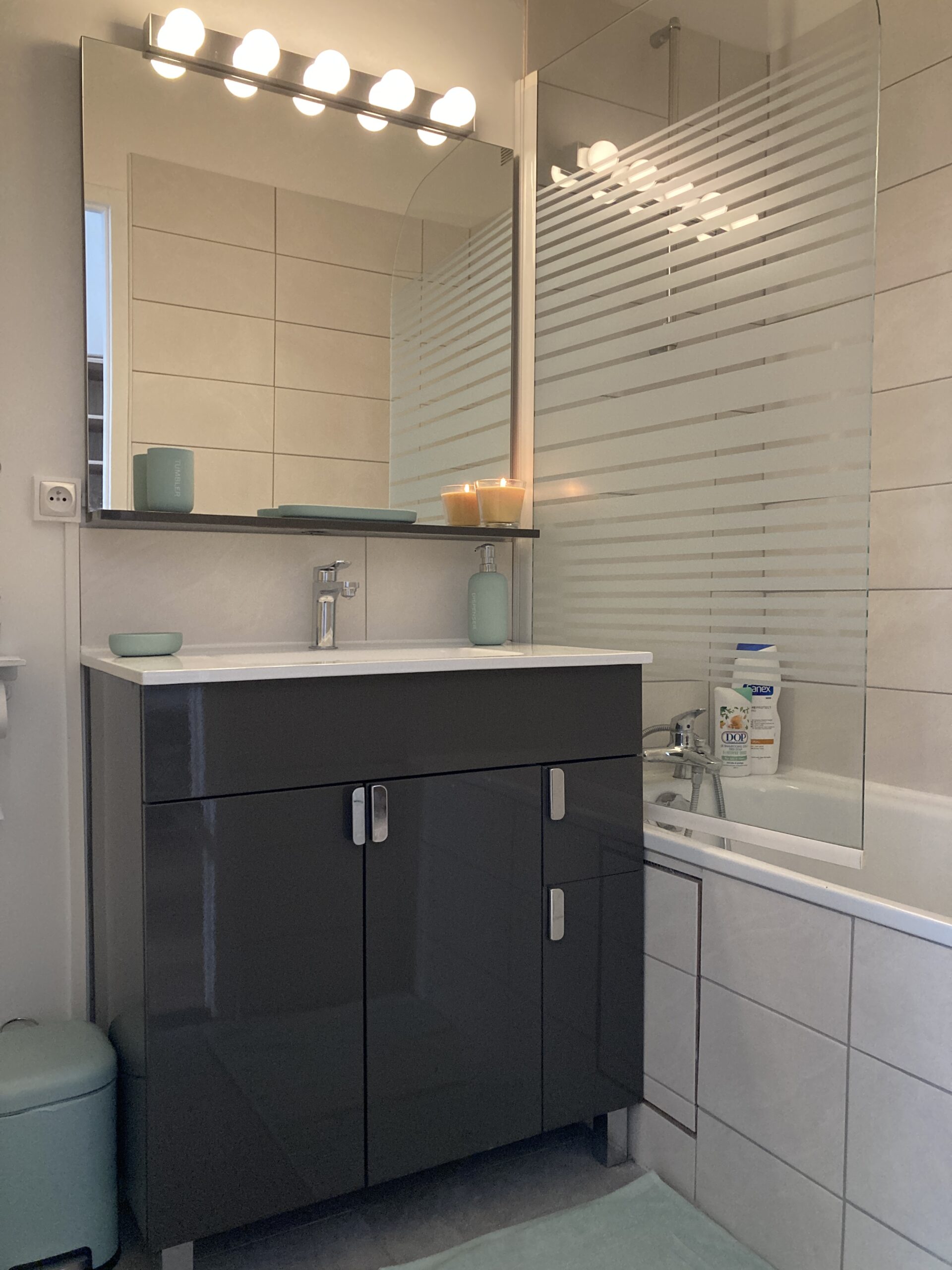 Plombier Rénovation Pierre-Bénite Oullins : nouvelle salle de bain avec meuble vasque incluant rangements, miroir moderne et éclairages, tablier de douche carrelé, et faïence murale neuve